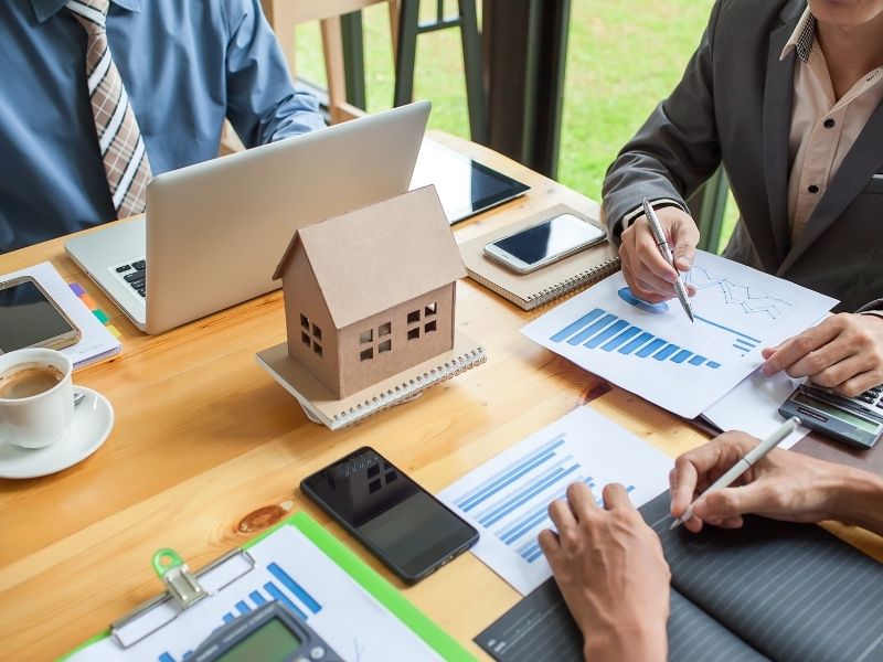 Mannen bespreken bouwkundige tekeningen bij maquette van woning, voor professioneel toezicht en directievoering